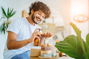 Happy hansome latin man holding glass bottle with dispenser and take care of his skin in home...