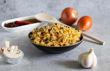 Pilaf with mushrooms and ingredients for it on a light concrete background