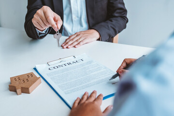 Sale Agent giving house keys to woman customer and sign agreement documents for realty purchase.