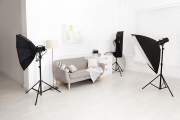 Set of stylish furniture surrounded by professional lighting equipment in photo studio. Cozy living room interior imitation