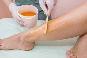 Shugaring concept. Beautician removes hair from client's legs with sugar paste.