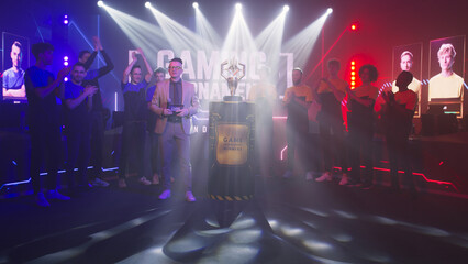 Host man speaking about golden cup while standing near cyber esportsmen at start of gaming tournament - obrazy, fototapety, plakaty