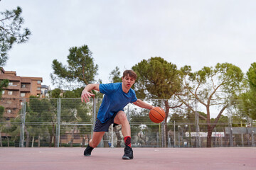 Obraz premium young athlete training outdoors. caucasian man playing basketball on a court, practicing dribbling with the ball.