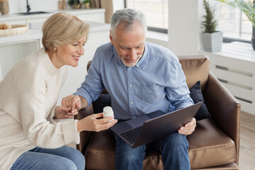 Smiling couple holding pills jar and laptop