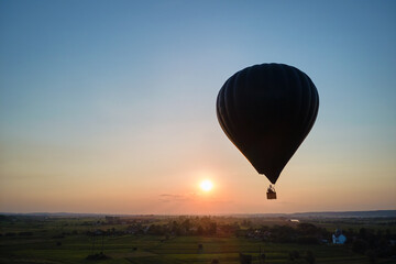 Aerial view of big hot air baloon flying over rural countryside at sunset