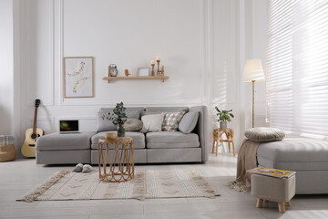 Living room with comfortable grey sofa, ottoman and stylish interior elements near window