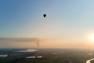 Aerial view of small hot air baloon flying over rural countryside at sunset