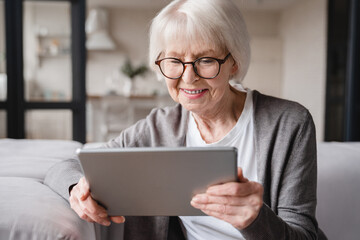 Caucasian beautiful old elderly senior woman lady grandmother using tablet for surfing social media, e-banking, e-commerce, checking pension, mortgage loan online at home