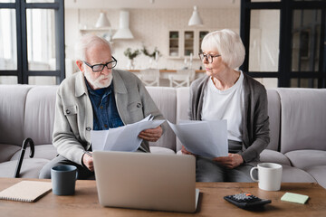 Serious elderly senior grandparents couple family wife and husband counting funds, savings, declarations, investments,paperwork, financial documents, bankruptcy, court case, bills, pension at home. - obrazy, fototapety, plakaty