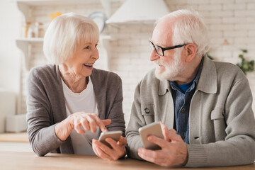 Smiling caucasian senior elderly couple grandparents spouses using smart phones cellphones...
