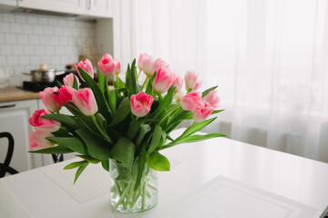 Bouquet of pink tulips in a transparent vase on the kitchen table. Flowers in the interior. International Women's Day 8 March.
