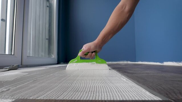 Worker Uses Scraper To Smear Glue On Floor Before Gluing Vinyl Or Laminate Tiles
