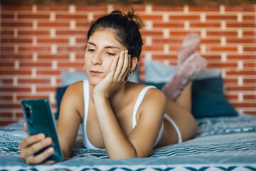 Young natural woman relaxing at home. Female texting on her smartphone while lying on the bed.