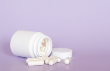Close up white pills and capsules on purple background with copy space. Focus on foreground, soft bokeh. Pharmacy drugstore concept.