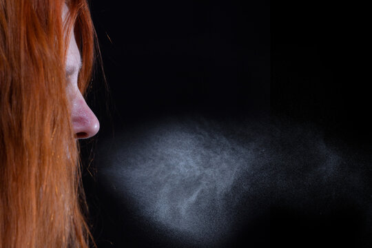 Porträt von einer rothaarigen Frau. Ihre Atemluft bildet eine Wolke von Aerosolen. Der Hintergrund ist ein dunkler Innenraum.