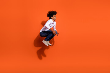 Photo of charming pretty guy dressed white shirt jumping diving empty space isolated orange color background