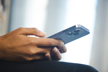 Black woman typing message on modern blue mobile phone with triple camera. Young adult African female using new smartphone for online communication