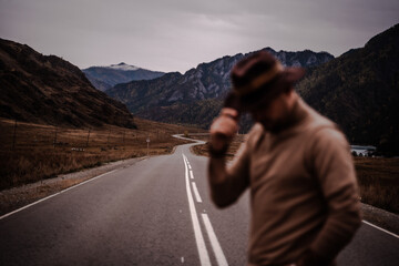 Young stylish guy in a hat stands on the background of a mountain road. Autumn. High quality photo