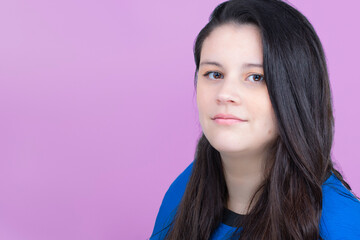 Young lady headshot. She is latin, in her thirties with long smooth hair. She is looking at the camera with a little smile and wears a blue top. The background is purple.