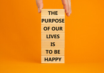 Purpose of happy lives symbol. Wooden blocks with words The purpose of our lives is to be happy. Beautiful orange background, copy space. Businessman hand. Business, purpose of lives is happy concept.