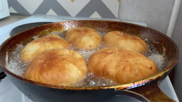 The cook fries pies belyashi stuffed with meat in a frying pan in oil