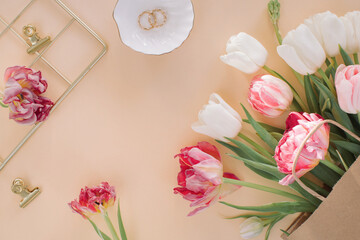 Set of feminine accessories, bunch of tulips in paper bag on beige background. Flat lay, top view minimal trendy fashion collage. Blogger and fashion concept. 