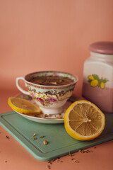 turquoise cup with flowers with green tea with lemon on and a ceramic tea jar on a pink background 