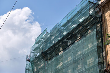 Building facade under renovation works with construction scaffolding frame covered with protective...