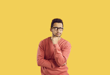 Hmm. Young student in glasses doubting something. Puzzled adult man in casual sweatshirt isolated on solid yellow background looking up and thinking hard about difficult question or future career plan