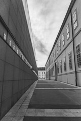 a narrow concrete road among the high facades of industrial buildings on the sides against a cloudy sky. Black and white photography