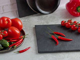 A dish with cucumber, chili peppers and tomatoes, next to a stone board with chili peppers, tomato and a knife on a light background. Kitchen. Plates. The working process. Selective focus.