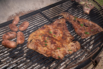 Barbecue outdoors. Closeup view of tri-tip, pork meat and sausages roasting in the grill.