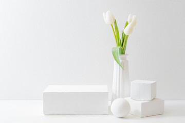 White podium for product display with white tulips in a vase on a light background