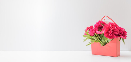 Beautiful gift box with red peonies on a white table with copy space. Concept of internet shopping,...