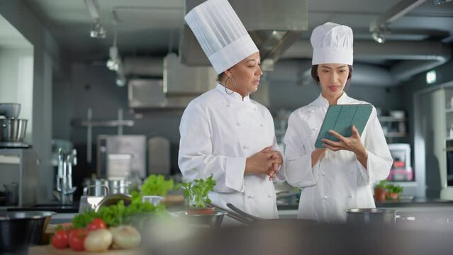 Restaurant Kitchen: Team of Asian and Black Female Chefs use Tablet Computer while Cooking Delicious and Authentic Food. Perfect Teamwork in Preparing Healthy Meal, Fusion Cuisine Dish