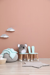 Child's toys, pouf and chairs near pink wall indoors. Interior design
