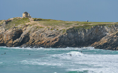 Ruine au sommet d'une falaise sur la côte sauvage de Quiberon en Bretagne. Quelques surfeurs affrontent les dangers de ce littoral tourmenté.