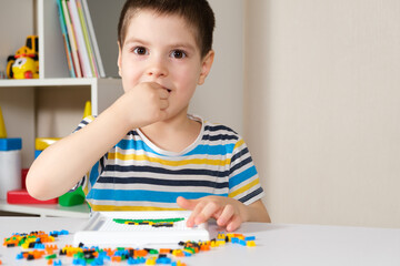 The child plays with mosaics, small objects for children, takes a small detail of the mosaic in his...