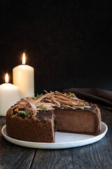 Fototapeta na wymiar Chocolate cheesecake or sponge cake in cut on a dark wooden table by candlelight.