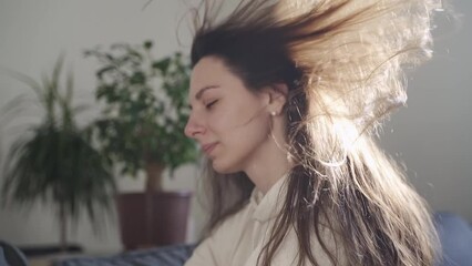 Young millennial woman blowing hair with hair dryer. Hot summer temperature at home. Using fan for cooling
