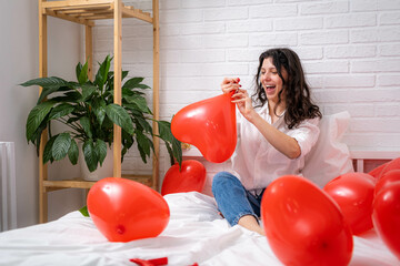 Girl is blowing air balloon at home Handsome brunette girl inflating red heart shaped balloon...