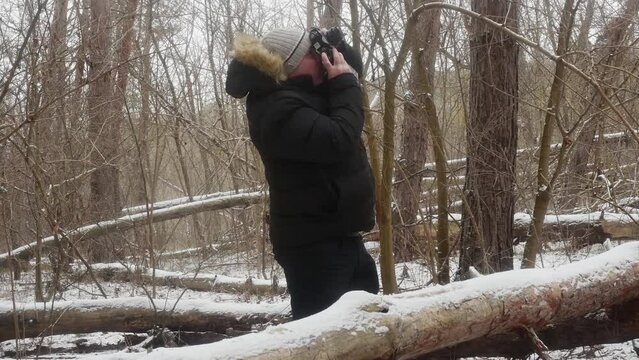 a man photographs nature on an old film camera among fallen trees in a snowy forest