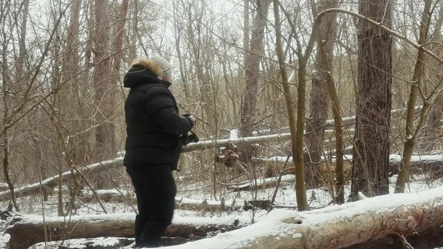 a man photographs nature on an old film camera among fallen trees in a snowy forest