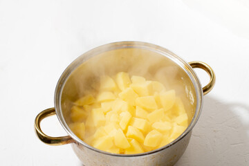 Boiled potatoes in a pot. Hot potato cubes with a piece of butter. Cooking boiled potatoes, mashed potatoes. Steam is coming. White background.