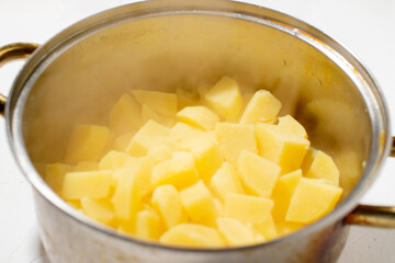 Boiled potatoes in a pot. Hot potato cubes with a piece of butter. Cooking boiled potatoes, mashed potatoes. Steam is coming. White background.