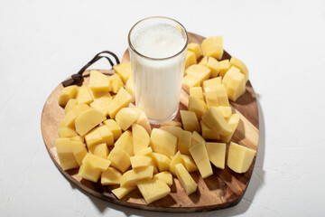 Potato milk concept. Alternative milk. A glass of milk on a wooden board with chopped raw potatoes.