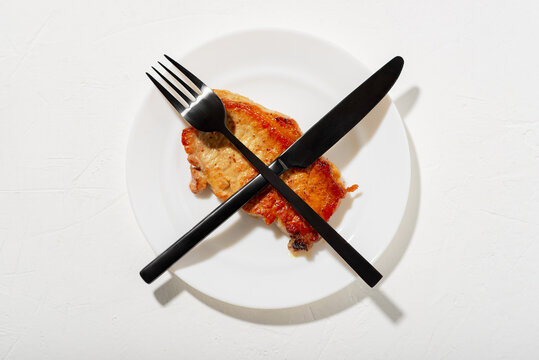 Stop meat concept. Stop eating animal products. A piece of fried meat crossed out with a fork and knife. White plate, background.