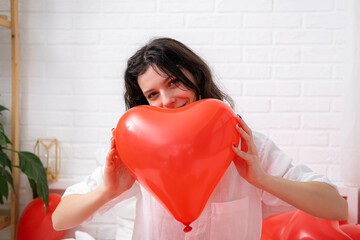 Red heart shaped balloon close up in hands of brunette smiling girl on Valentines Day