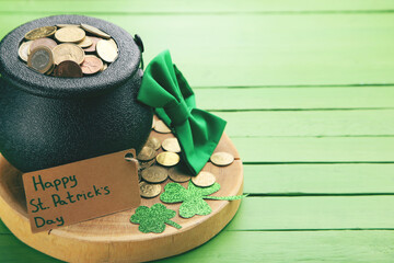 Pot of coins, bow tie, clover leafs and tag with text Happy St.Patrick's Day on green wooden...