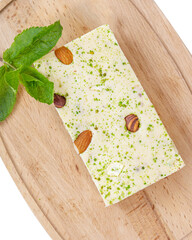 A piece of halva with almonds on a wooden board, decorated with mint leaves, on a white background. top view. National sweets, national cuisine concept